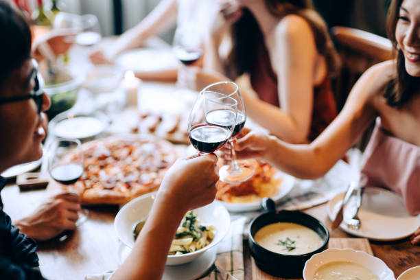 Close up of young Asian man and woman enjoying together, having fun and toasting with red wine during party with a group of friends