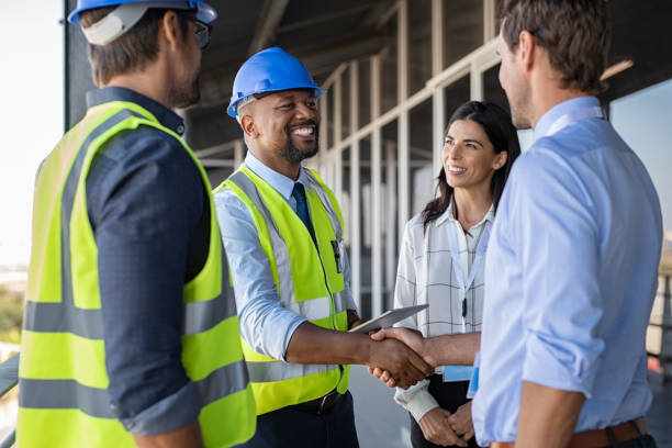 Engineer and businessman handshake at construction site Smiling engineer shaking hands at construction site with happy architect. Handshake between cheerful african construction manager with businessman at bulding site. Team of workers with architects and contractor conclude an agreement with safety uniform. building contractor stock pictures, royalty-free photos & images