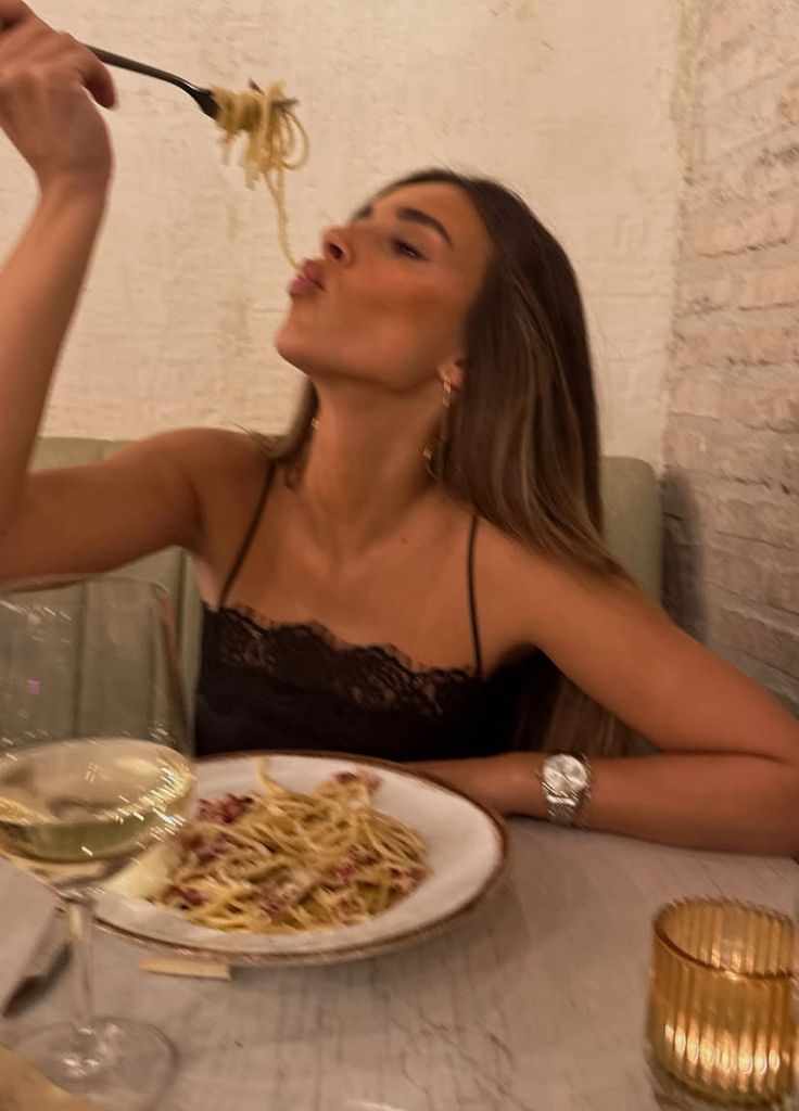 This may contain: a woman sitting at a table eating spaghetti