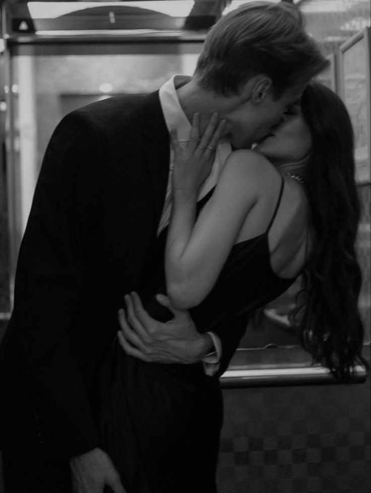 This may contain: a man and woman kissing in front of a glass case with their hands on each other