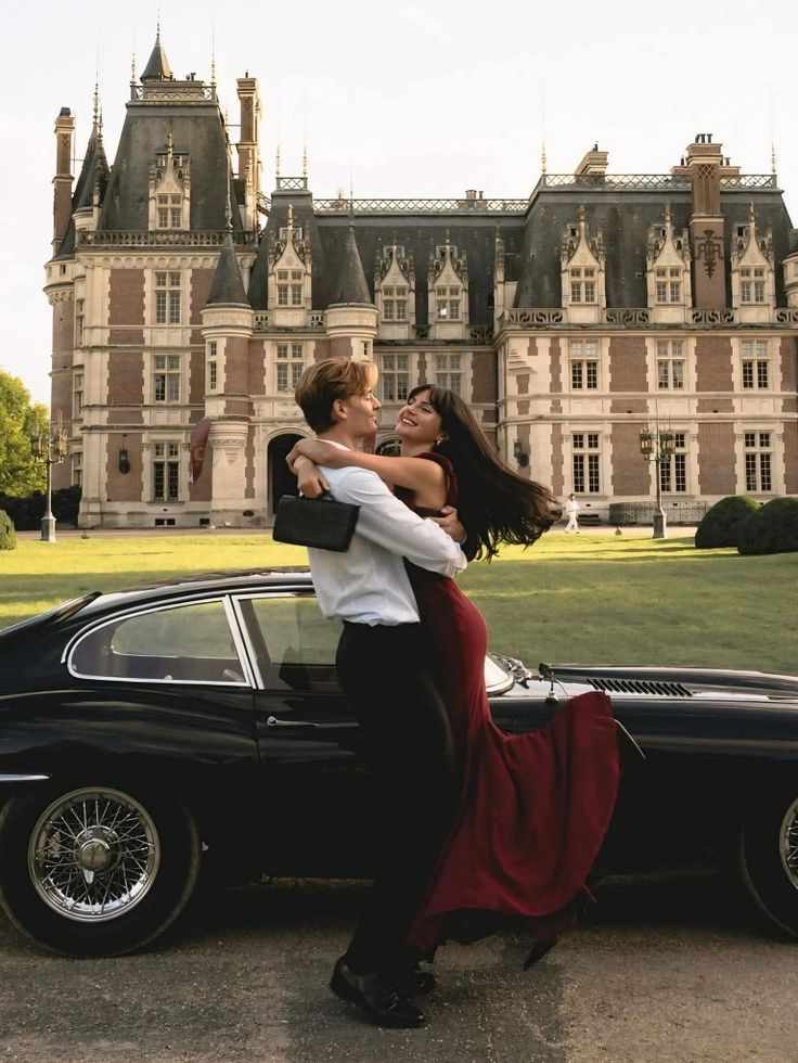 This may contain: a man and woman standing next to a car in front of a castle