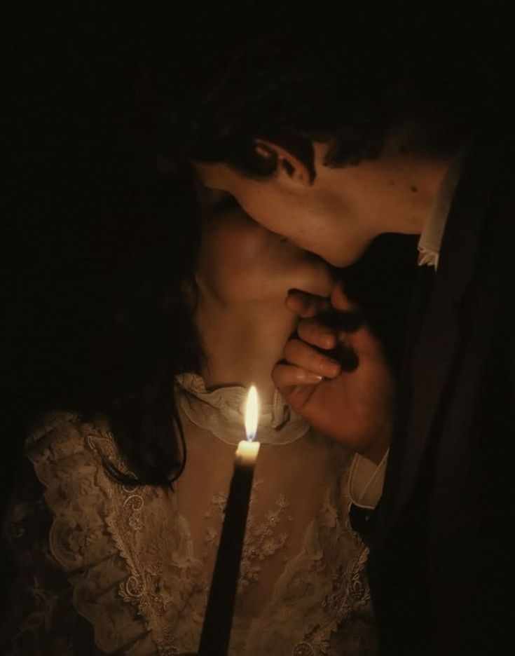 This may contain: a man and woman kissing in the dark with a lit candle between their hands as they stand close to each other