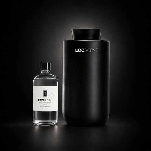 A matte black cylindrical EcoScent diffuser stands next to a clear glass bottle with a white label on a dark studio background.