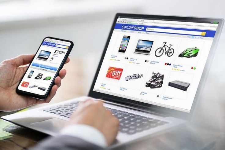 This may contain: a person holding a cell phone in their hand while looking at the website on his laptop