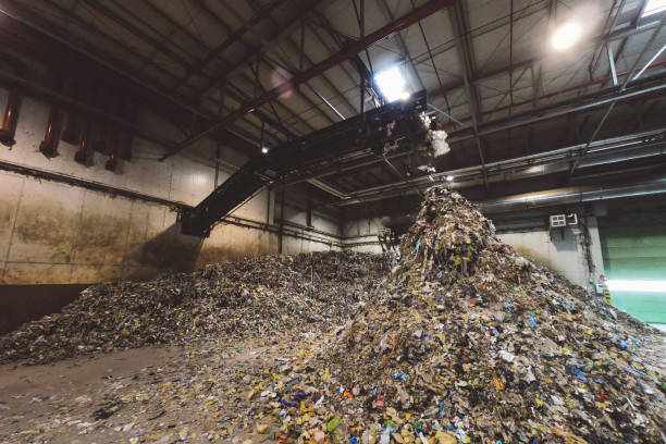 Shredded plastic falling off conveyor belt forming a pile Huge piles of shreded plastic waste ready for recycling inside the waste recycling facility.  Biomining of Legacy Waste  stock pictures, royalty-free photos & images