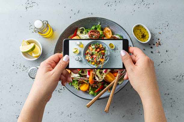Woman taking photo of vegetable salad with smartphone. Posting food pictures (images) on social media. Woman taking photo of fresh, spring, vegetable salad with smartphone. Using phone while eating lunch. Lifestyle trend - posting and sharing food pictures (images) on social media. Restaurant Marketing stock pictures, royalty-free photos & images
