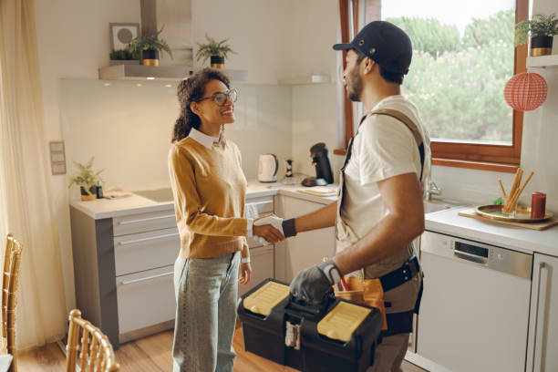 Professional repairman in uniform shaking hands with woman while standing at home kitchen Professional male handyman shaking hands with happy female client while standing at home kitchen plumbing stock pictures, royalty-free photos & images