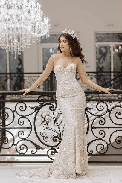 studio photo of a girl in a wedding dress near a black metal railing. A large hanging chandelier. Luxury interior in white style studio photo of a girl in a wedding dress near a black metal railing. A large hanging chandelier. Luxury interior in white style Milanova Bridal dress stock pictures, royalty-free photos & images