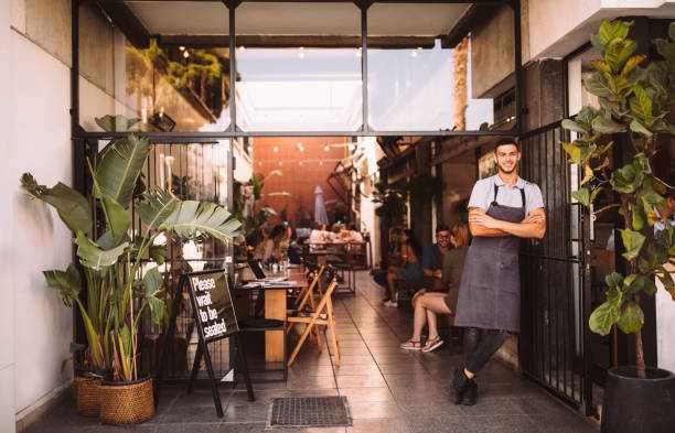 Young male business owner standing outside hipster urban café Young male manager and business owner standing at the entrance of modern urban restaurant business franchises stock pictures, royalty-free photos & images