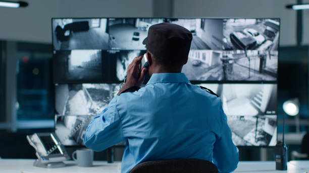 Back view of African-American security officer in system control room answer phone call Back view of African-American security officer in system control room answer phone call cctv surviellance stock pictures, royalty-free photos & images
