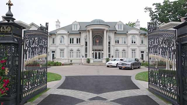 This may contain: two cars are parked in front of a large house with an iron gate that leads to the driveway