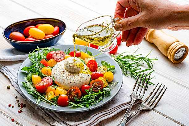 Female hand pouring olive oil on a burrata and tomato salad plate. Healthy Mediterranean diet. Traditional Italian meal. Raw food diet. Fresh and juicy ingredients or tasty snack Female hand pouring olive oil on a burrata and tomato salad plate. Healthy Mediterranean diet. Traditional Italian meal. Raw food diet. Fresh and juicy ingredients or tasty snack Organic Farm-to-Table Restaurant stock pictures, royalty-free photos & images