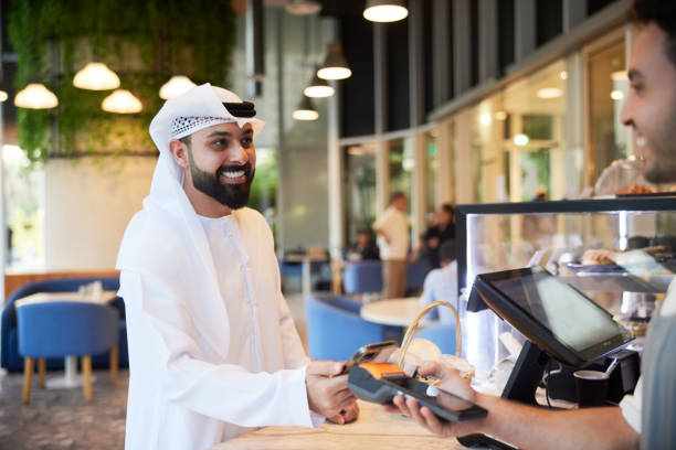 The coffee shop waiter is all set to charge a client with the POS system after serving the order. At the coffee shop, the client taps their phone on the dataphone, completing the contactless payment. restaurant in dubai stock pictures, royalty-free photos & images