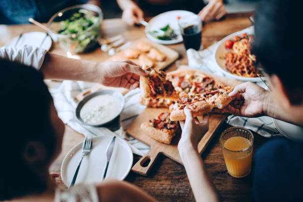 Close up of a young group of friends passing and serving food while enjoying together. They are having fun, chatting and feasting on food and drinks at dinner party Close up of a young group of friends passing and serving food while enjoying together. They are having fun, chatting and feasting on food and drinks at dinner party pizza stock pictures, royalty-free photos & images